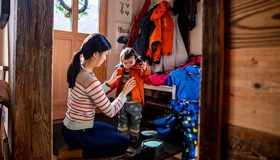 Mom helping daughter with winter jacket in mudroom